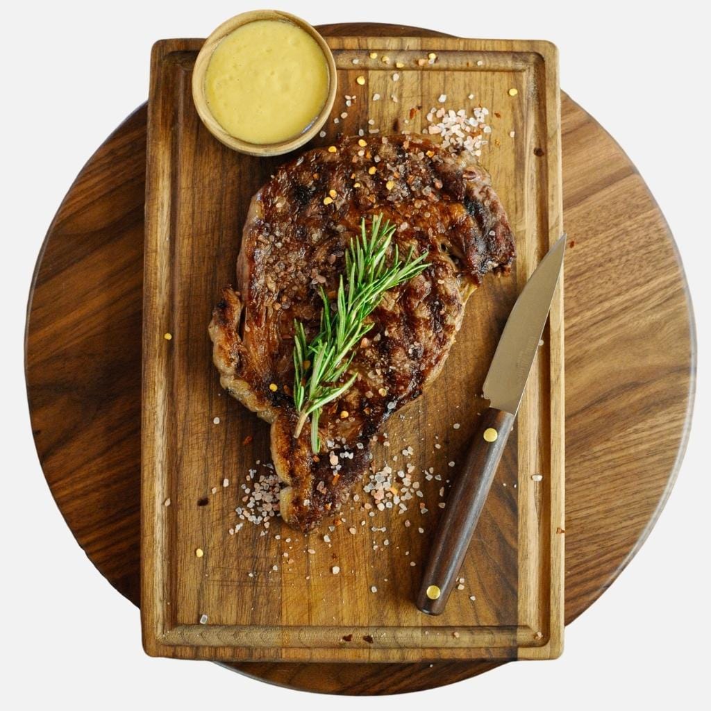 top view of cooked ribeye and a knife on top of walnut cutting board for hinoki vs walnut cutting board