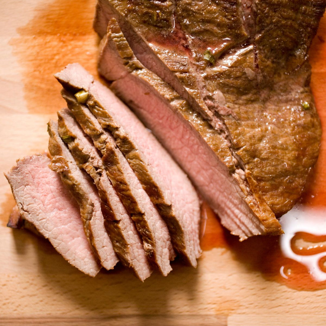 top view of sliced reverse sear london broil on top of a wood cutting board
